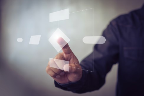 Person interacting with a digital flowchart on a transparent touchscreen interface, representing system design and architecture
